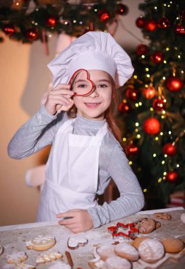 Şefin şapka şovlarındaki neşeli kız Noel arkaplanındaki Noel kurabiyelerine bakıyor.