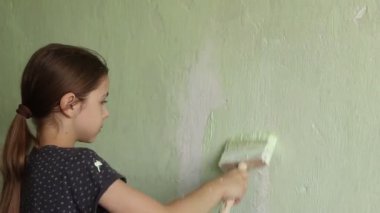 Çekici küçük bir kız dairede tadilat yapıyor. Duvarı fırçayla boyuyor.