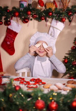 Neşeli bir kız gözlerini Noel ağacı şeklinde zencefilli kurabiyelerle kapatıyor.