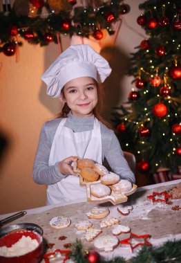 Bir kız Noel arkaplanındaki Noel ağacı şeklinde bir tabakta kurabiye tutuyor. Aile Noel kurabiyesi yapıyor