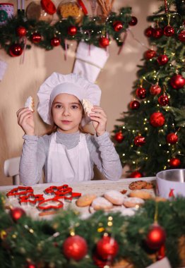 Aşçı şapkalı bir kız gülümser ve Noel ağacı şeklinde zencefilli kurabiye gösterir..