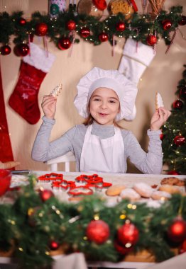 Şefin şapkasıyla neşeli bir kız Noel ağacı şeklinde zencefilli kurabiye gösteriyor.
