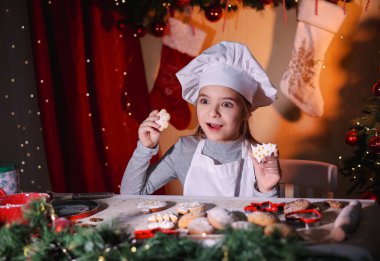 Şefin şapkasıyla neşeli bir kız Noel ağacı şeklinde zencefilli kurabiye gösteriyor.