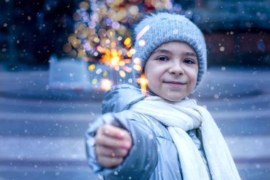 Kış akşamında bir Noel ağacının arka planında maytap tutan küçük bir kız. Tatiller, çocukluk ve insanlar konsepti