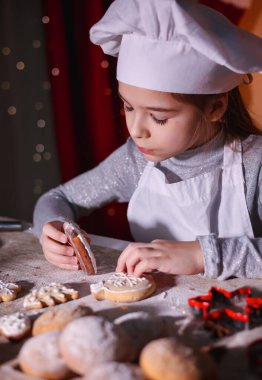 Şef gibi giyinmiş bir çocuk tatil için zencefilli kurabiyeleri dikkatlice süslüyor..