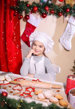 Neşeli Noel sezonunda aşçı gibi giyinmiş gülümseyen kız kurabiye hazırlıyor.