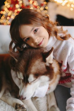 Noel arkaplanında iri kıyım köpeğe sarılan tatlı bir kız..