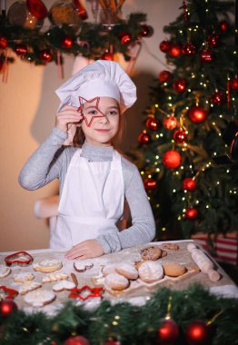 Şefin şapka şovlarındaki neşeli kız Noel arkaplanındaki Noel kurabiyelerine bakıyor.