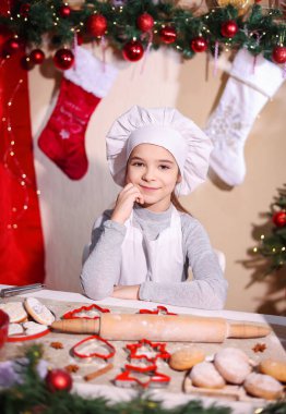 Neşeli Noel sezonunda aşçı gibi giyinmiş gülümseyen kız kurabiye hazırlıyor.