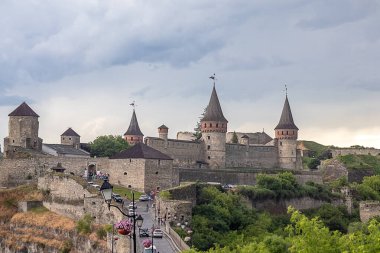 Ortaçağ kalesi yeşilliklerle çevrili ve bulutlu bir gökyüzü tarihi cazibe sergiliyor. Kamianets-Podilskyi Eski Kalesi, Ukrayna 'nın tarihi kenti Kamianets-Podilskyi' de yer almaktadır..