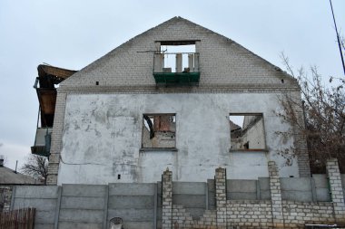 İhmal edilmiş, duvarları hasarlı, camları kırık ve etrafı çorak bir tuğla bina..