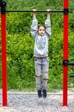 Kız barfiks egzersizi yapıyor. Spor, açık hava aktivitesi ve sağlıklı yaşam tarzını ön plana çıkarıyor..