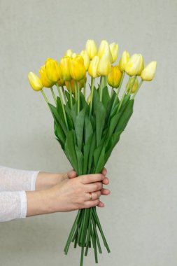 Canlı sarı lalelerden oluşan bir buket nazikçe tutulmuş, tazeliği ve zarafeti simgeliyor..