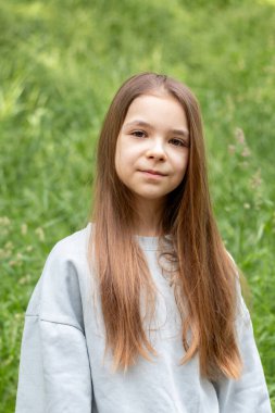 Açık havada yeşil bir yerde duran genç bir kızın portresi..