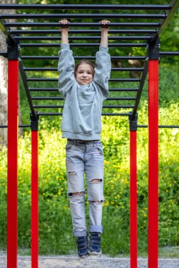 Gülümseyen genç kız dışarıda oyun parkı parmaklıklarında fiziksel aktivite gösteriyor.