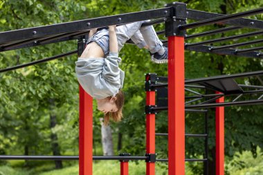 Yeşil yapraklarla çevrili açık hava barlarında asılı duran bir kız.
