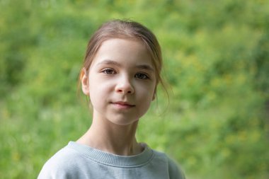 Arka planda yeşillikle kameraya bakan genç bir kız.