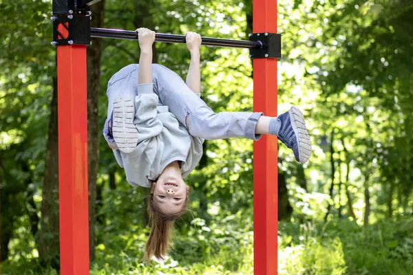 Yatay bir barda asılı duran genç bir kız doğa ile çevrili açık hava aktivitelerinin keyfini çıkarıyor.