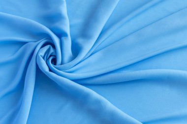 Parlak açık mavi kumaşın ayrıntılı bir yakın çekimi sanatsal olarak katlanmış ve bükülmüş..