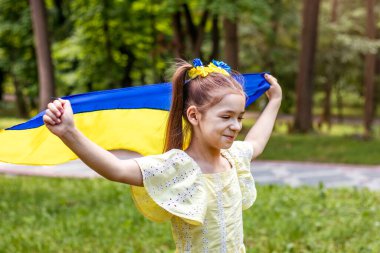 Sarı ve mavi çiçekli bir çelenk içindeki bir kız Ukrayna bayrağını elinde bir tarlanın arka planında tutuyor. Ukrayna Bağımsızlık Bayrak Günü.
