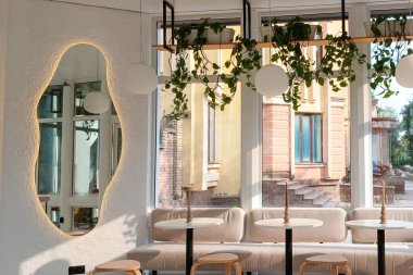 Büyük pencerelerden sarkan fabrikalar, modern mobilyalar ve güneş ışığı görünen bir kafe..