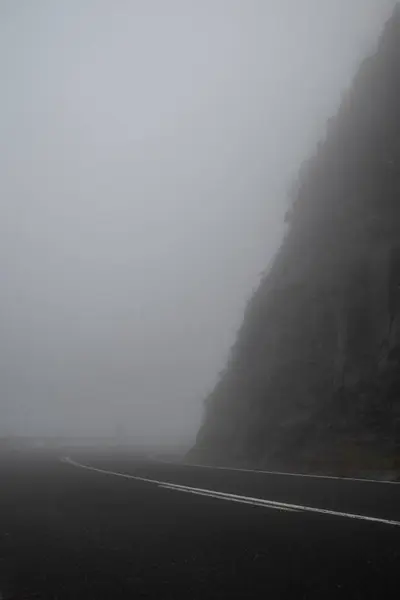 Foggy mountain road with a curve and dark silhouette of a person in the background. Concept of unknown future, mystery and unpredictability. Dark autumn mountain road. Hiking through foggy mountains