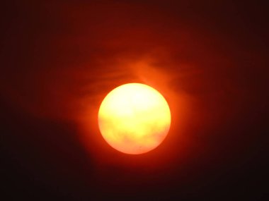 Güneşin ışıltılı görüntüsü kızıl bir gökyüzünü aydınlatıyor, sakin bir atmosfer manzarası yaratıyor..