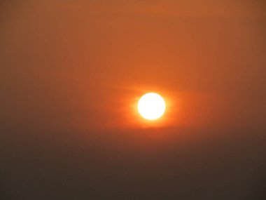 Güneşin parlak görüntüsü kahverengi gökyüzünü aydınlatıyor, sakin bir atmosfer manzarası yaratıyor..
