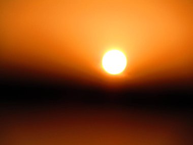 Güneşin parlak görüntüsü kahverengi gökyüzünü aydınlatıyor, sakin bir atmosfer manzarası yaratıyor..