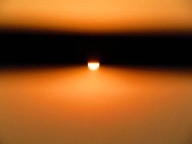 Güneşin parlak görüntüsü kahverengi gökyüzünü aydınlatıyor, sakin bir atmosfer manzarası yaratıyor..