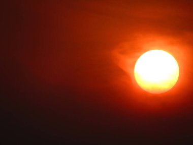 Güneşin ışıltılı görüntüsü kızıl bir gökyüzünü aydınlatıyor, sakin bir atmosfer manzarası yaratıyor..