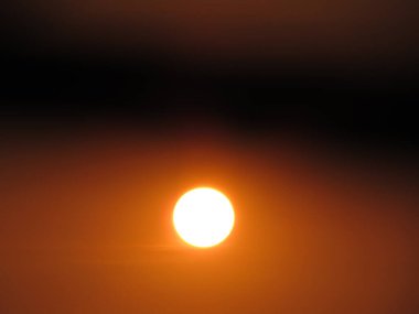 Güneşin parlak görüntüsü kahverengi gökyüzünü aydınlatıyor, sakin bir atmosfer manzarası yaratıyor..