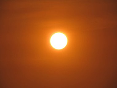 Güneşin parlak görüntüsü kahverengi gökyüzünü aydınlatıyor, sakin bir atmosfer manzarası yaratıyor..