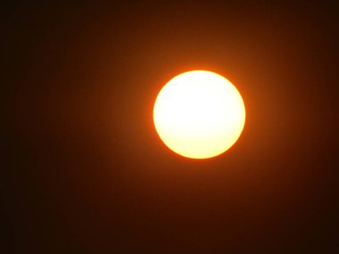 Güneşin ışıltılı görüntüsü gri gökyüzünü aydınlatıyor, sakin bir atmosfer manzarası yaratıyor..