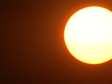 Güneşin ışıltılı görüntüsü gri gökyüzünü aydınlatıyor, sakin bir atmosfer manzarası yaratıyor..