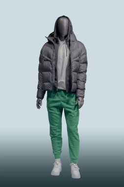 Mavi arka planda siyah örtülü ceket ve yeşil yün pantolon giyen bir erkek vitrin mankeni.