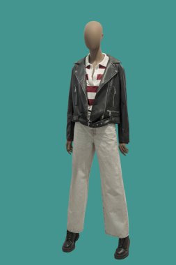 Siyah deri ceket ve yeşil arka planda izole edilmiş gri kot giyen bir kadın vitrin mankeni.