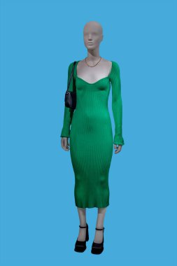 Full length image of a female display mannequin wearing fashionable green knitted dress isolated on blue background