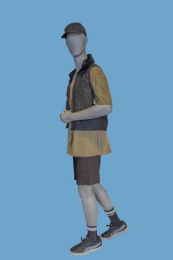 Full length image of a male display mannequin wearing brown vest with hood; t-shirt and shorts isolated on blue background