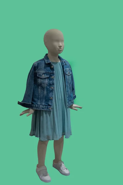 青いジーンズのジャケットと緑の背景に隔離されたライトブルーのプリーツドレスを身に着けている子供ディスプレイマネキンの完全な長さの画像 — ストック写真