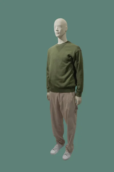 緑の背景に隔離された緑のプルオーバーとライトブラウンのパンツを身に着けている男性ディスプレイマネキンの完全な長さの画像 — ストック写真