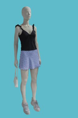 Yeşil arka planda siyah ve mavi etek giymiş bir kadın vitrin mankeninin tam boy görüntüsü