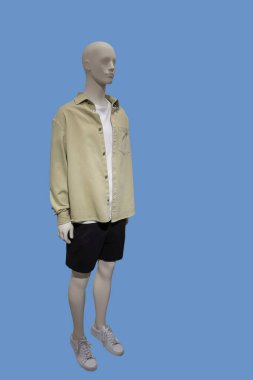 Yeşil arka planda düğmesiz gömlek ve siyah şort giyen bir erkek vitrin mankeninin tam boy görüntüsü