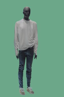 Yakasız beyaz gömlek ve yeşil arka planda izole edilmiş kot pantolon giyen bir erkek vitrin mankeni.