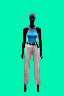Yeşil arka planda mavi kolsuz üst ve beyaz kot giyen bir kadın vitrin mankeni tam boy görüntüsü