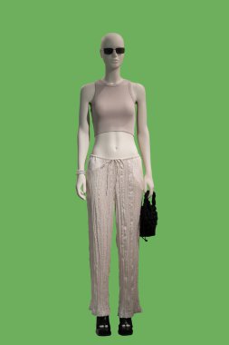 Açık kahverengi örgü bluz ve yeşil arka planda izole edilmiş beyaz renkli pantolon giymiş bir kadın vitrin mankeni.