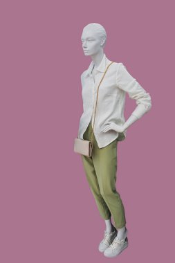 Pembe arka planda beyaz gömlek ve haki rengi pantolon giyen bir kadın vitrin mankeni.