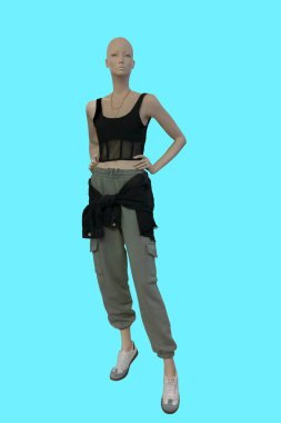 Mavi arka planda izole edilmiş, yeşil kargo pantolon ve siyah bluz giyen bir kadın vitrin mankeni.