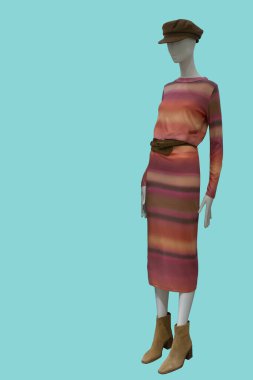 Yeşil arka planda uzun kollu bir elbise giyen bir kadın vitrin mankeni.