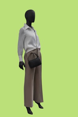 Modaya uygun beyaz bluz ve yeşil arka planda izole edilmiş açık kahverengi pantolon giyen bir kadın vitrin mankeni.